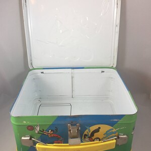 May include: A vintage metal lunchbox featuring a colorful design of Mickey Mouse and Goofy playing sports. The lunchbox has a yellow handle and a white interior with a divider.
