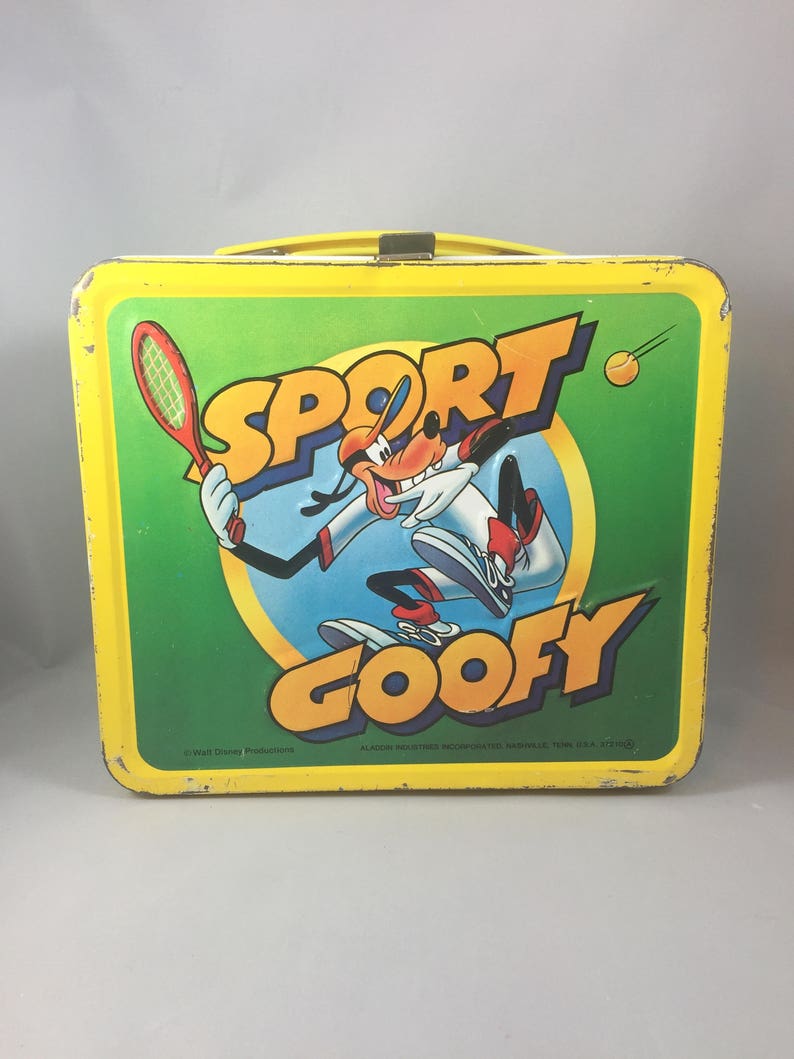 May include: A yellow metal lunchbox with a green background featuring Goofy playing tennis. The lunchbox has the words "Sport Goofy" on it.