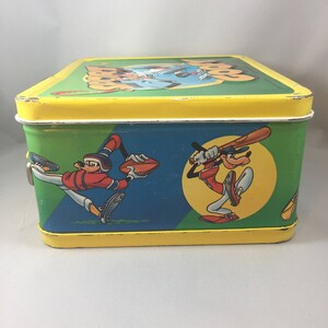 May include: A vintage yellow metal lunchbox with a green, blue, and yellow design featuring cartoon characters playing baseball. The lunchbox has a latch on the side and the text "Goofy" on the top.