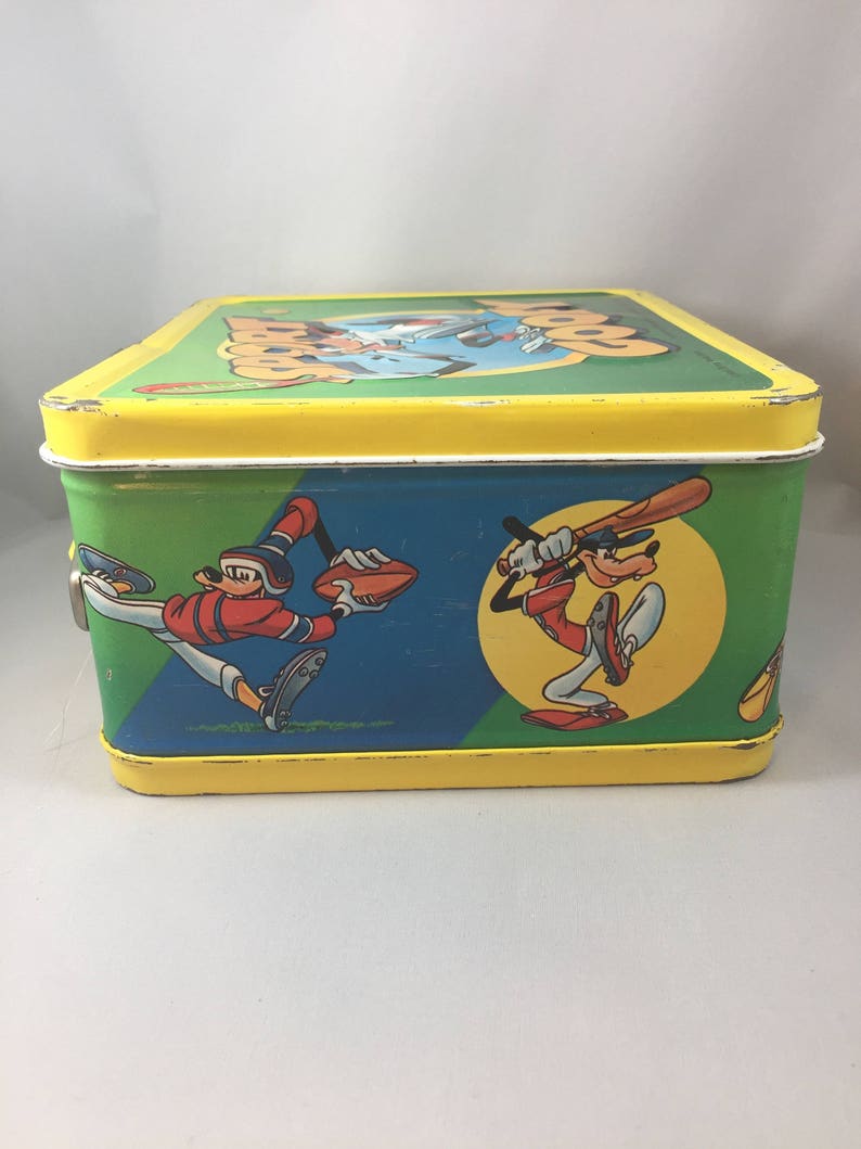 May include: A vintage yellow metal lunchbox with a green, blue, and yellow design featuring cartoon characters playing baseball. The lunchbox has a latch on the side and the text "Goofy" on the top.