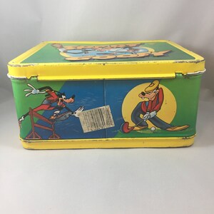 May include: A yellow metal lunchbox with a green, blue, and white image of Goofy playing golf and running a hurdle race. The lunchbox has the words "Goofy Goofy" on the top.