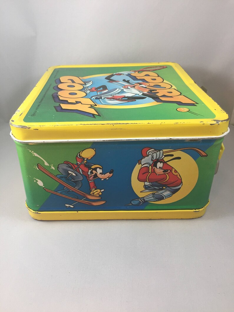May include: A yellow metal lunchbox with a green, blue, and yellow design. The lunchbox features a cartoon image of Goofy and Mickey Mouse skiing and playing baseball. The text "Sport Goofy" is printed on the top of the lunchbox.