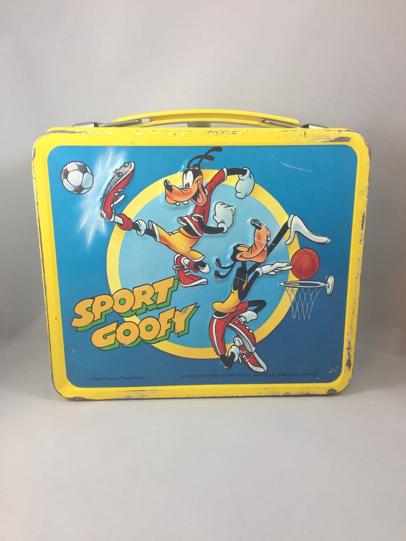 May include: Yellow metal lunchbox featuring Goofy and a cartoon version of himself playing sports. The lunchbox has the words "Sport Goofy" on the front.