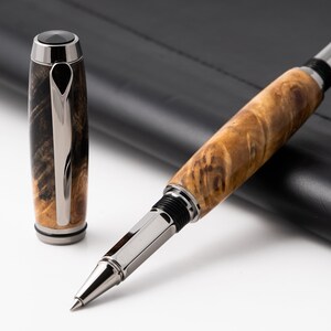 Puede incluir: Un bolígrafo roller de madera marrón y negro con una punta de metal plateado y una libreta de cuero negro.
