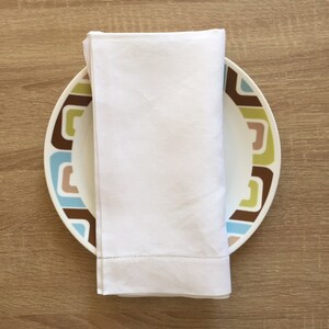 May include: A white linen napkin folded and placed on a white plate with a brown, blue, green, and beige geometric pattern.
