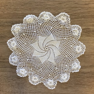 May include: White crocheted doily with a spiral design in the center. The doily has a scalloped edge and is made of delicate lace.