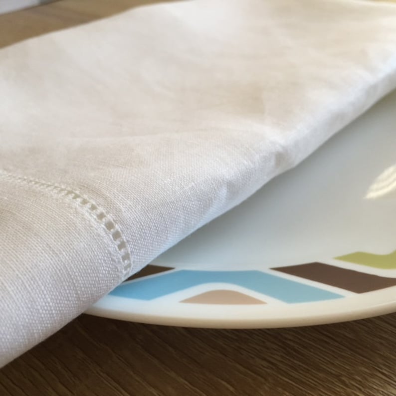May include: A white linen napkin folded over a white plate with a colorful geometric design. The plate has brown, blue, and green accents.