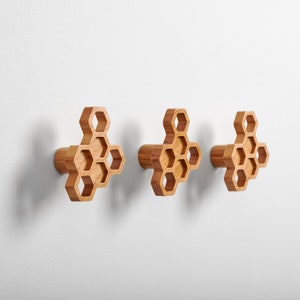 May include: Three wooden wall hooks shaped like a honeycomb. The hooks are light brown and have a natural wood finish.