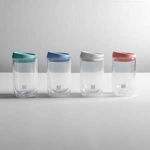 May include: Four double-walled glass mugs with lids in different colours: teal, blue, white, and pink. Each mug has the word "B&Uuml;" printed on the bottom.