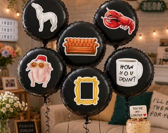 May include: Black round balloons with stickers of a white dog, a red lobster, a brown couch, a turkey wearing sunglasses, a yellow picture frame, and a white mug with "How You Doin'?" text. A cake with the text "You're my lobster" is also visible.