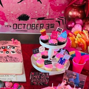K&ouml;nnte beinhalten: Eine rosa Party-Dekoration mit Kuchen, Cupcakes und verschiedenen Leckereien. Der Kuchen ist mit Text und Zeichnungen verziert. Cupcakes sind mit rosa Zuckerguss und thematischen Dekorationen versehen. Der Hintergrundtext lautet "It's October 3rd".