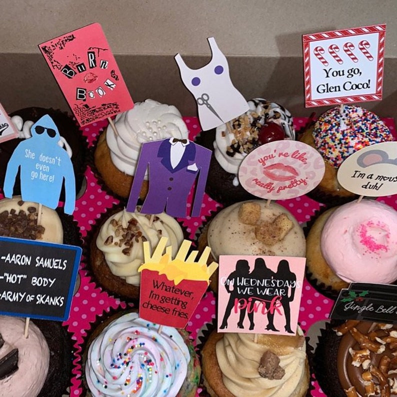 K&ouml;nnte beinhalten: Eine Schachtel mit dekorierten Cupcakes mit verschiedenen Aufs&auml;tzen. Aufs&auml;tze sind ein pinkes "Burn Book", ein blauer Pullover mit Text, ein lila Anzug, ein wei&szlig;es Kleid und S&auml;tze wie "You go, Glen Coco!" und "On Wednesdays We Wear Pink".