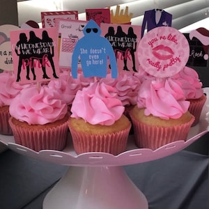 K&ouml;nnte beinhalten: Eine Sammlung von Cupcakes mit rosa Zuckerguss, pr&auml;sentiert auf einem wei&szlig;en, mehrst&ouml;ckigen Servierst&auml;nder. Die Cupcakes sind mit verschiedenen Toppern verziert, darunter Silhouetten, eine blaue Kapuzenpullover-Grafik mit Text und ein rosa Lippen-Design mit Text.