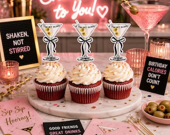 May include: Three red velvet cupcakes topped with white frosting and martini-themed decorations. The cupcakes are on a marble serving plate, with cocktail napkins and olives nearby. The sign says "Birthday Calories Don't Count."