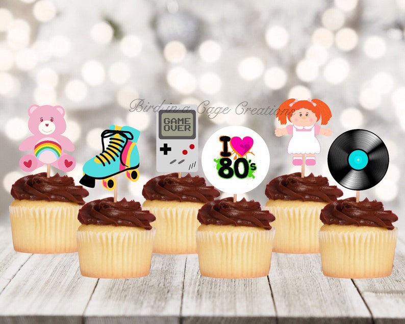 May include: Set of 8 cupcake toppers featuring 1980s themed designs. The toppers include a pink Care Bear, roller skates, a game over screen, a record, a Cabbage Patch doll, and a circle with the text "I Love 80's".
