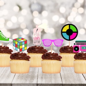 May include: A set of 8 cupcake toppers featuring 80s themed designs. The toppers include a green sneaker, a Rubik's cube, a pink and blue boombox, a pair of pink sunglasses, a spray can with the text "Big Hair Don't Care", and a colourful circle with a black centre.