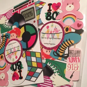 May include: A set of 1980s themed party props, including a pink Care Bear, a rainbow, a record player, a Rubik's Cube, roller skates, and a hairspray bottle with the text "Big Hair Don't Care".