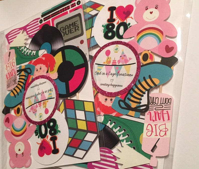 May include: A set of 1980s themed party props, including a pink Care Bear, a rainbow, a record player, a Rubik's Cube, roller skates, and a hairspray bottle with the text "Big Hair Don't Care".