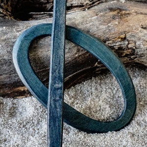 Könnte beinhalten: Ein dunkelblauer Holzhaarstecker mit abgerundeter Spitze und einem passenden dunkelblauen Holzring. Der Haarstecker und der Ring liegen auf einer weißen Oberfläche.