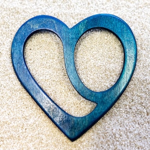 Könnte beinhalten: Holzherz-Dekoration mit blauem Farbverlauf. Das Herz hat ein ausgeschnittenes Design, das einen offenen Raum innerhalb der Herzform schafft. Es liegt auf einer strukturierten, hellfarbigen Oberfläche.