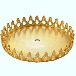 May include: Gold metal round cake stand with a decorative crown-like edge. The stand has a hole in the center.