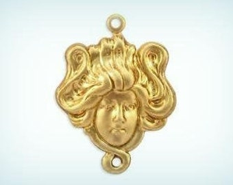 May include: A gold-toned pendant featuring a detailed, stylised face of a woman with flowing hair. The pendant has two loops for attaching a chain.