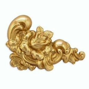 May include: A gold-colored decorative corner piece with a rose and scrollwork design.