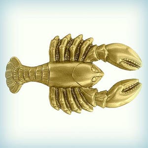 May include: A detailed, golden-colored lobster figurine. The crustacean is depicted with intricate details, including claws, segmented body, and a fan-shaped tail. The lobster is positioned horizontally against a gradient blue and white background.
