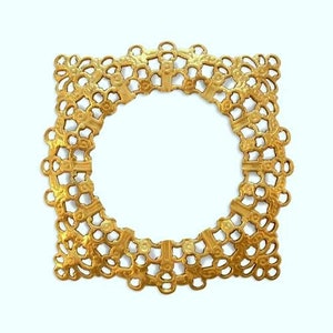 May include: Gold-toned metal frame with a square shape and intricate, decorative details. The frame has a circular opening in the center.