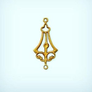 May include: A gold-colored, ornate metal pendant with a symmetrical design. The pendant features a stylized, elongated shape with a central vertical element and decorative flourishes. It has a loop at the top and bottom for attachment.