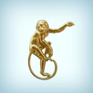 May include: A gold-colored monkey figurine with a curled tail, sitting on its haunches and pointing with its right hand.