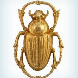 May include: A gold-colored scarab beetle sculpture with intricate details. The beetle is depicted with wings outstretched and a detailed body.