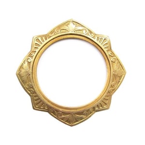May include: A gold-toned, ornate, circular frame with a starburst design. The frame has a decorative, intricate pattern.