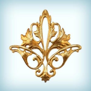 May include: A gold-colored metal decorative ornament with a floral design. The ornament has a symmetrical design with intricate details and a delicate, filigree-like appearance.