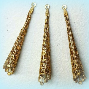 K&ouml;nnte beinhalten: Drei goldfarbene, konisch geformte Schmuckteile aus Filigran. Jeder Konus hat ein offenes Design mit komplizierten floralen und geometrischen Mustern. Die Teile haben oben eine kleine Schlaufe zur Befestigung an anderen Schmuckkomponenten. Die Konen sind etwa 5 cm lang.