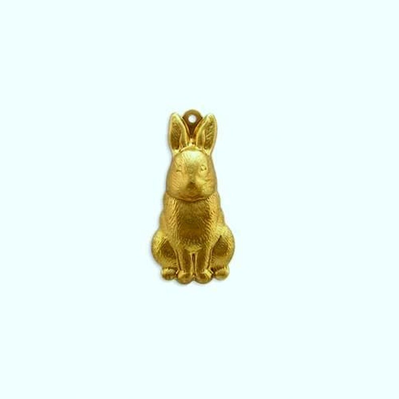 May include: A gold-colored metal charm in the shape of a sitting rabbit. The rabbit has a detailed, textured surface.
