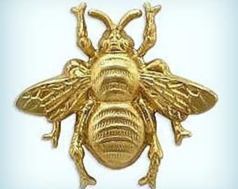 May include: A gold-colored metal bee figurine with detailed wings and legs. The bee is in a flying position with its wings spread out.