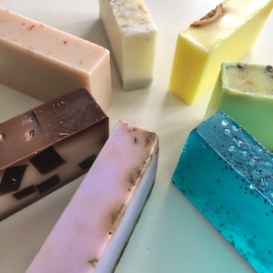 May include: Assortment of handmade soap bars in various colors and textures. The bars include brown, beige, light purple, light green, light blue, and yellow.