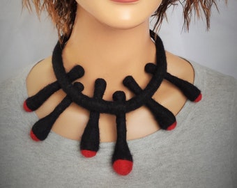 May include: A black felt necklace with a unique design. The necklace features a thick, rounded collar with several black, teardrop-shaped pendants. Each pendant has a red tip, creating a striking contrast against the black felt.