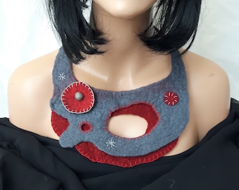May include: A gray and red felt necklace with a unique design. The necklace features a gray base with red accents, including a large circular element and smaller decorative details. A silver-colored button is in the center of the large circular element.