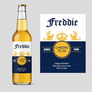 Può includere: Una bottiglia di birra in vetro con un'etichetta personalizzata che riporta il nome Freddie, una corona e due creature alate. Il testo recita Cheers to 30, Since 1995 e Happy Birthday! With lots of love from Mum & Dad in blu navy, bianco e oro.