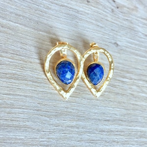 以下が含まれることがあります： 中心に青い宝石がついた、涙の形をしたデザインの金色のイヤリングです。