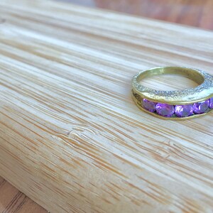 Puede incluir: Un anillo de oro con una fila de piedras preciosas púrpuras engastadas en una banda texturizada.