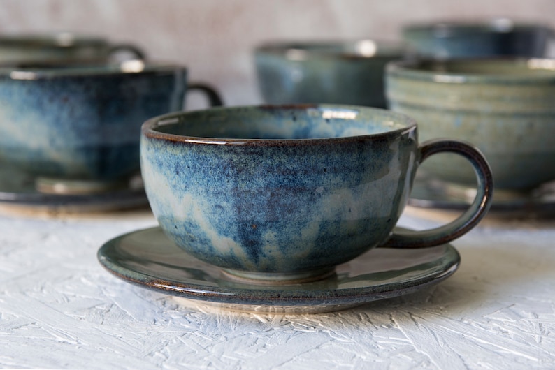 May include: A set of blue and white ceramic teacups and saucers. The cups have a speckled glaze and a rounded shape. The saucers are a matching blue and white.