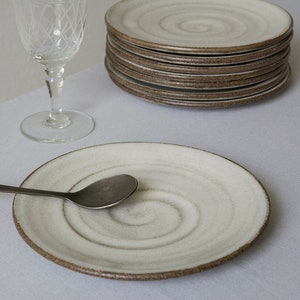 Puede incluir: Un plato de cer&aacute;mica blanco con un dise&ntilde;o en espiral y un borde marr&oacute;n. Una cuchara de plata descansa sobre el plato. El plato est&aacute; sobre un mantel blanco.