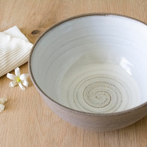 May include: A white ceramic bowl with a brown rim and a swirling pattern on the inside. The bowl is sitting on a wooden surface.