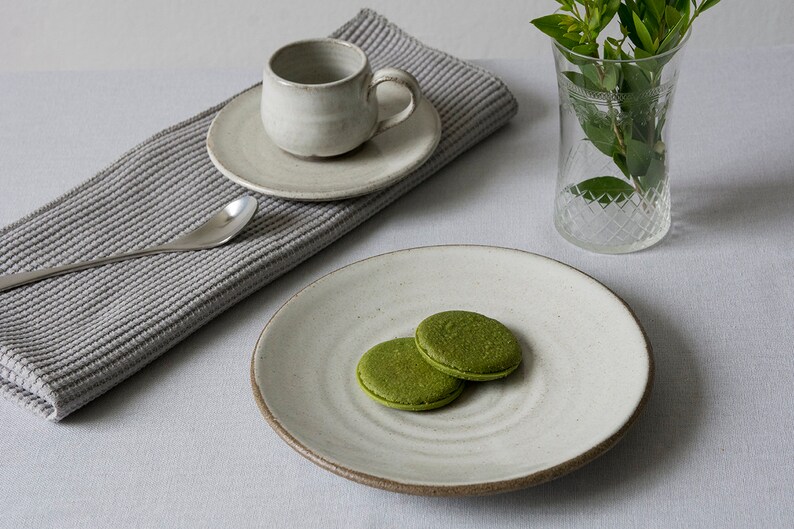 Puede incluir: Dos galletas de matcha verdes en un plato de cer&aacute;mica blanco sobre un fondo blanco. El plato tiene un dise&ntilde;o de espiral.
