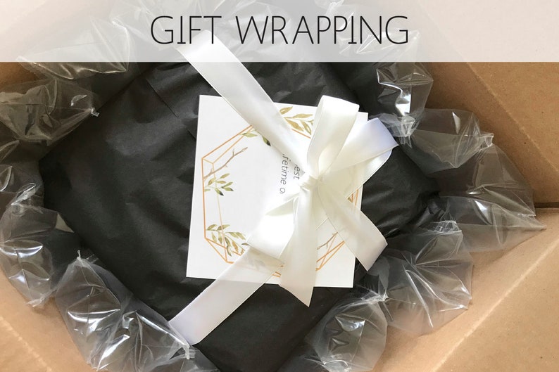 Op de afbeelding: Een cadeau verpakt in zwart tissuepapier met een wit lint en een kaart met de tekst "De beste tijd is een leven lang" in een gouden geometrisch frame.