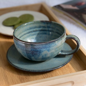 May include: A blue and white ceramic teacup and saucer set on a wooden tray. The teacup has a textured, speckled glaze.