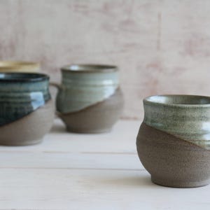 Puede incluir: Cuatro tazas de cerámica con un esmalte marrón y verde. Las tazas tienen un cuerpo redondeado y un asa.